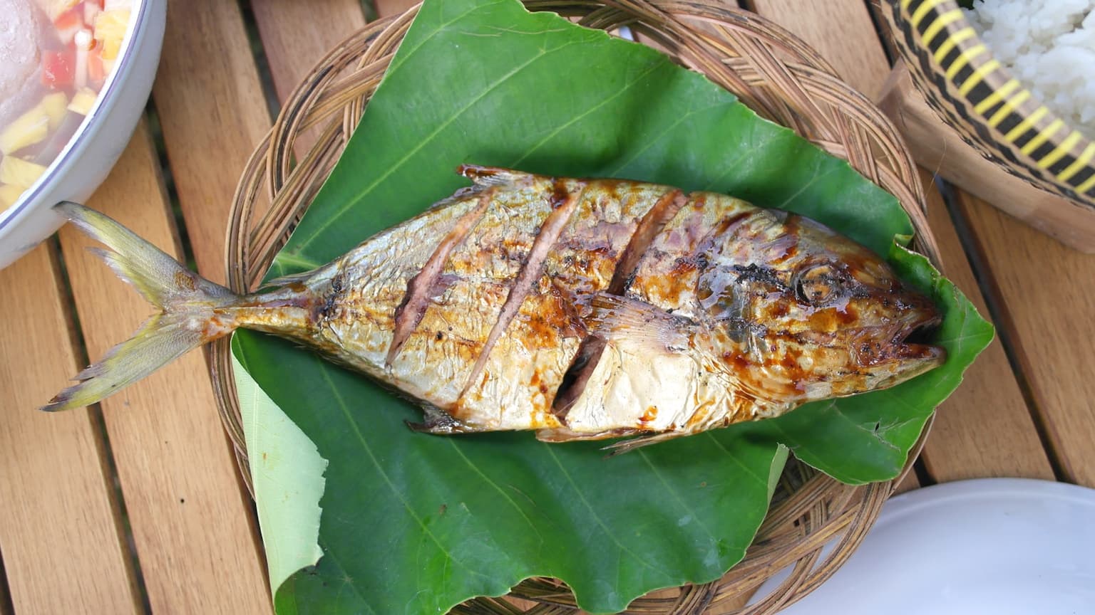 A scored grilled fish plated on a green leaf